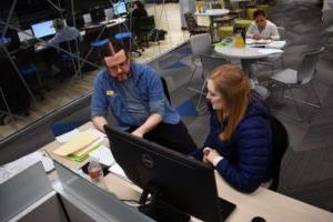 student and tutor talk while sitting at a computer station